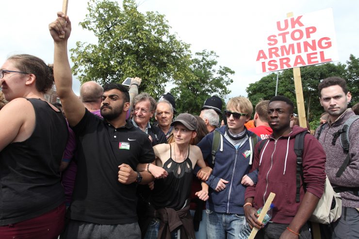 Protesters linking arms and holding a placard saying "UK stop arming Israel"