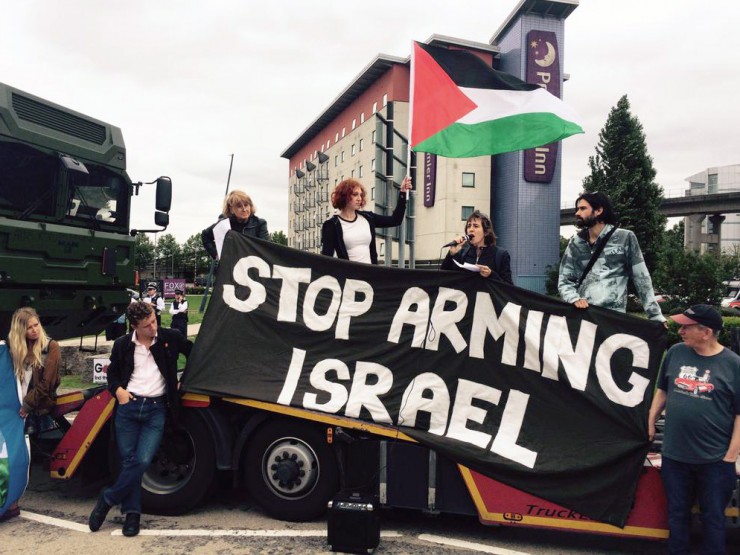 Activists occupy a flatbed truck displaying a "Stop Arming Israel" banner and Palestinian flag